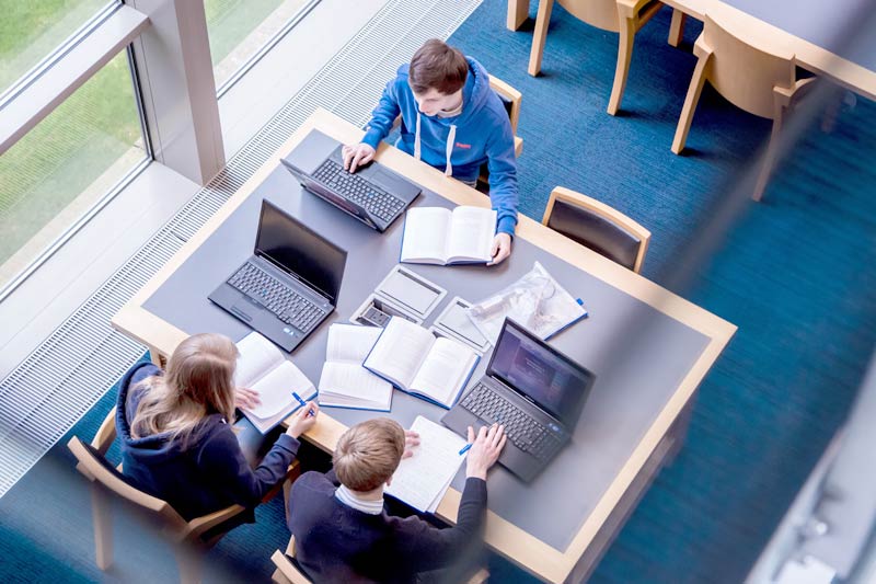birdesye view of three students working on laptops at a desk in the McClay library